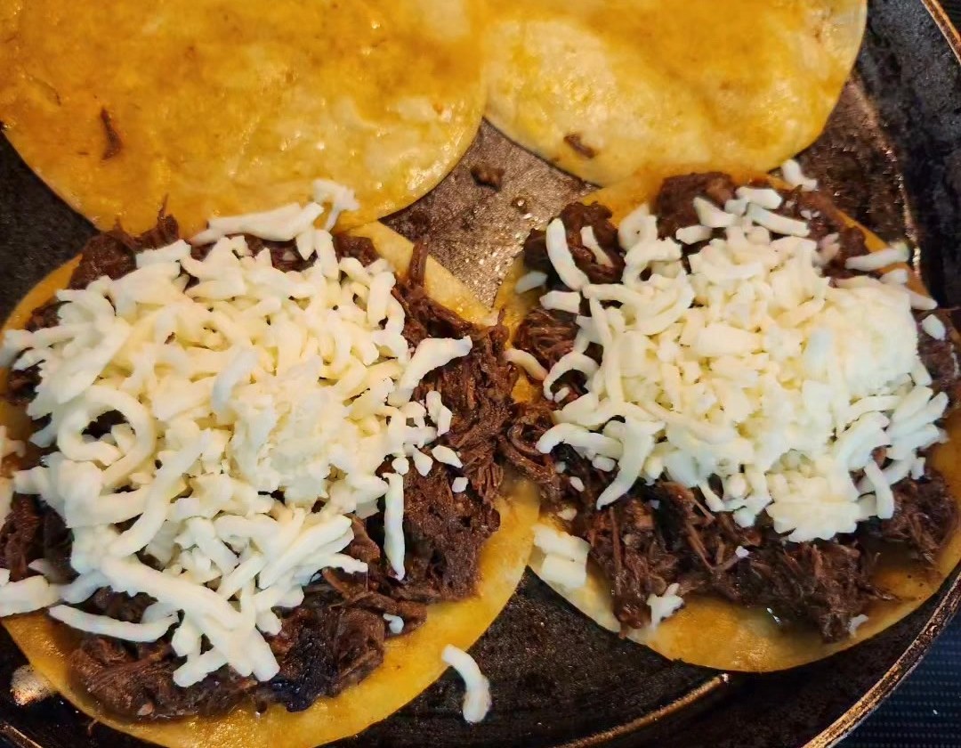 Birria quesadillas on a skillet, loaded with shredded beef and melted cheese.