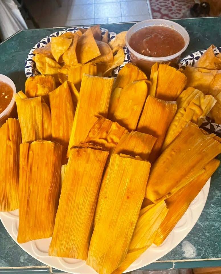A full platter of homemade tamales in their corn husks, served with tortilla chips and salsa.
