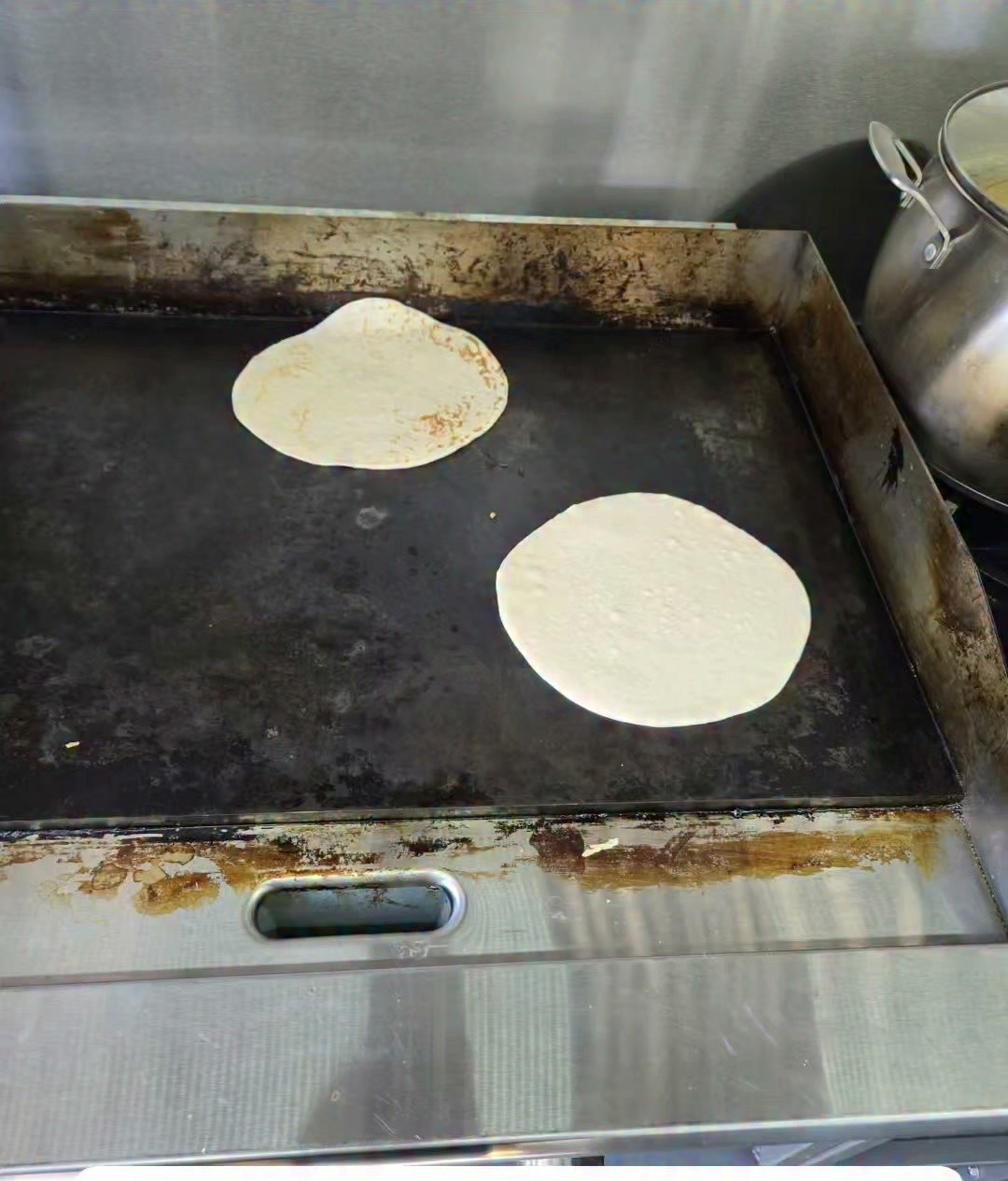 Two tortillas puffing up on the hot flat-top griddle inside the food truck.